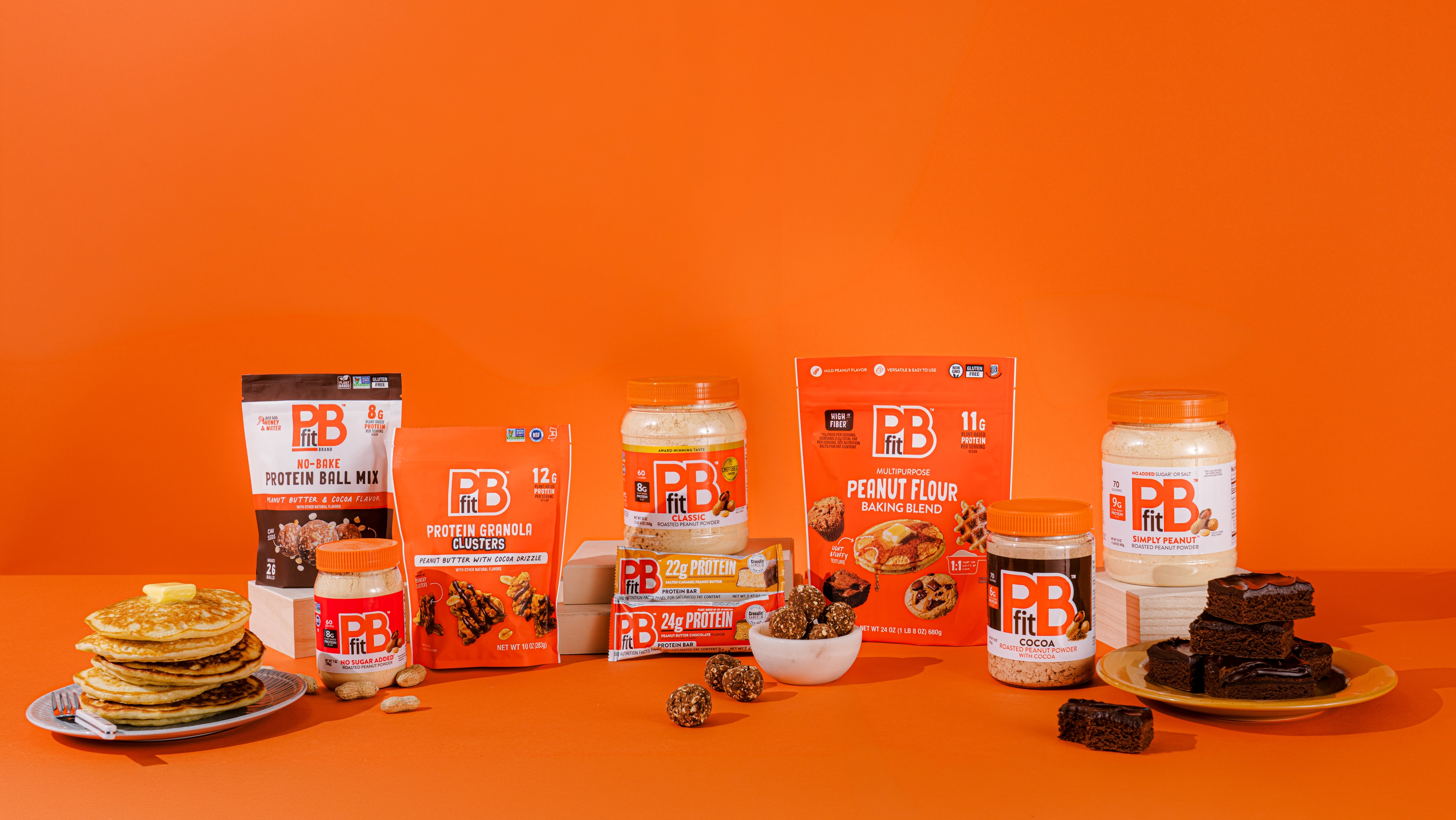 PBfit Classic surrounded by pancakes, smoothies, protein balls, cookies, and more. 