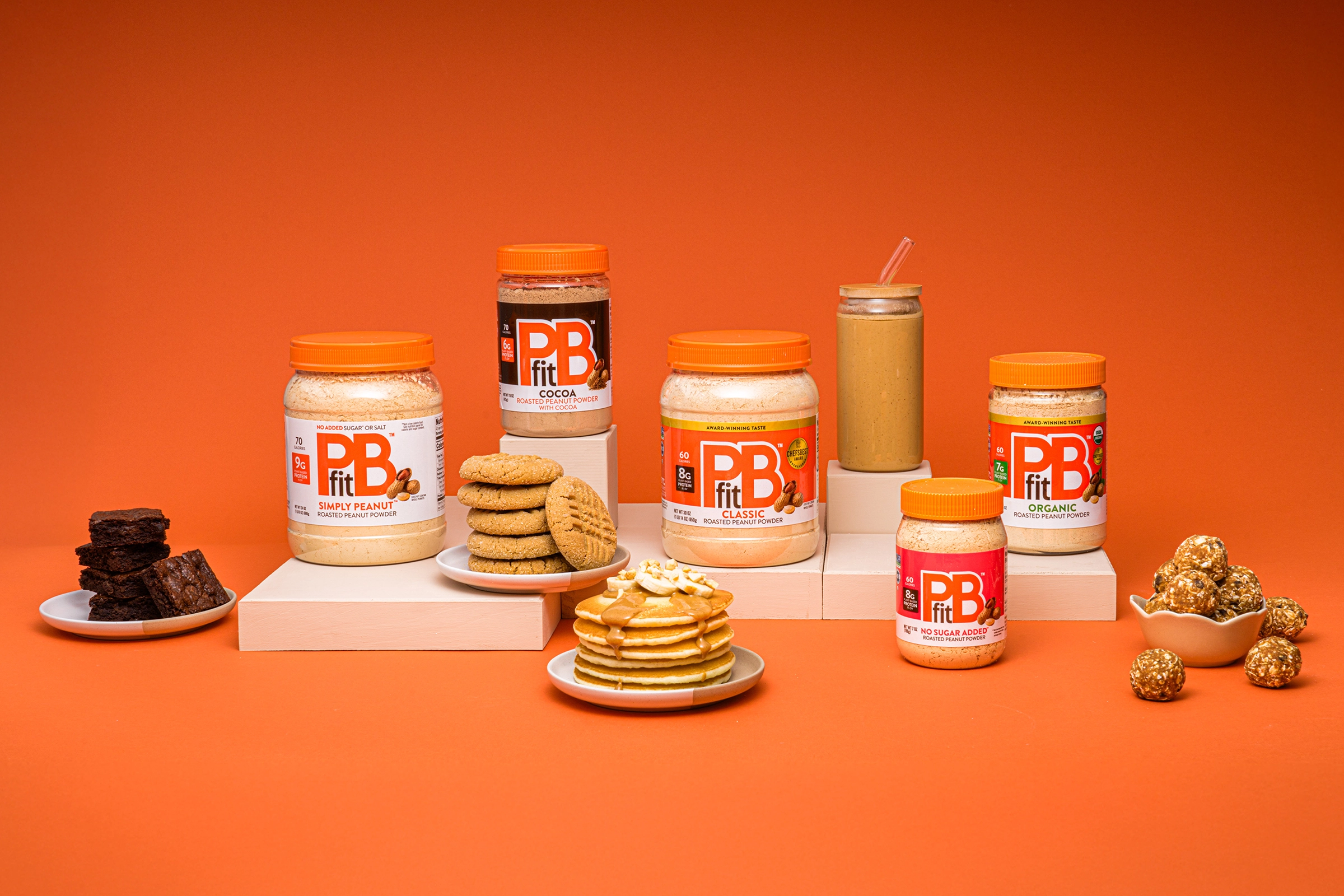 PBfit Classic surrounded by pancakes, smoothies, protein balls, cookies, and more.